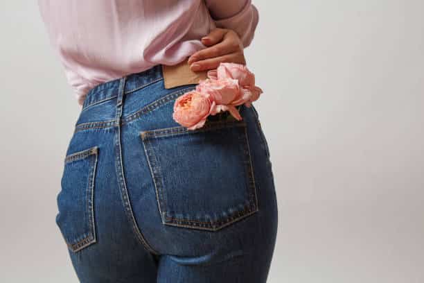 Fondo de mujer perfecto en jeans azules y rosas frescas color coral vivo en un bolsillo trasero sobre un fondo gris claro, lugar para el texto. Concepto del Día de la Mujer o de la Madre.