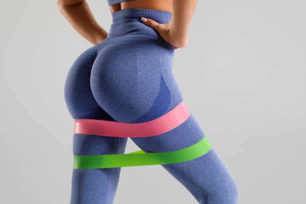 Fitness woman doing exercise for glutes with resistance band on gray background. Beautiful buttocks, athletic girl working out