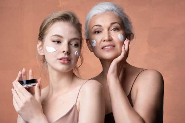Aging and skincare routine. Two female generations mature mother, young adult daughter with jar applying moisturizing sunscreen cream on skin together. Women care skin by nourishing beauty cosmetics.