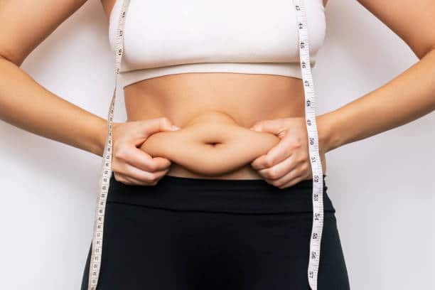 Cropped shot of a young woman with measuring tape around the neck holding herself by the fat on her stomach isolated on a white background. Overweight, excess weight concept