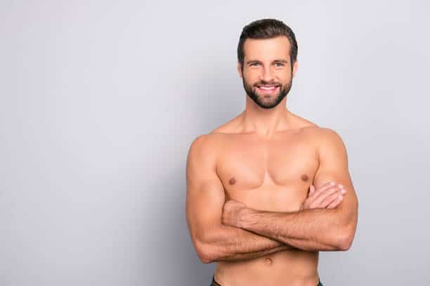Portrait with copy space of attractive, virile, harsh, sporty, manly, stunning man with crossed arms, muscular, naked torso, looking at camera, isolated on gray background