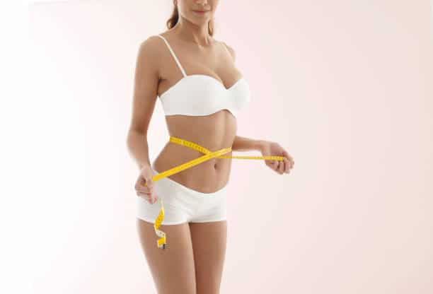 Close up of woman measuring hips with tape measure.